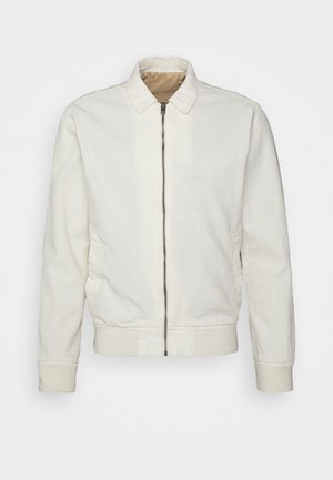 Veste blanche zippée avec col, poignets et ceinture côtelés, montrée de face sur un fond uni.