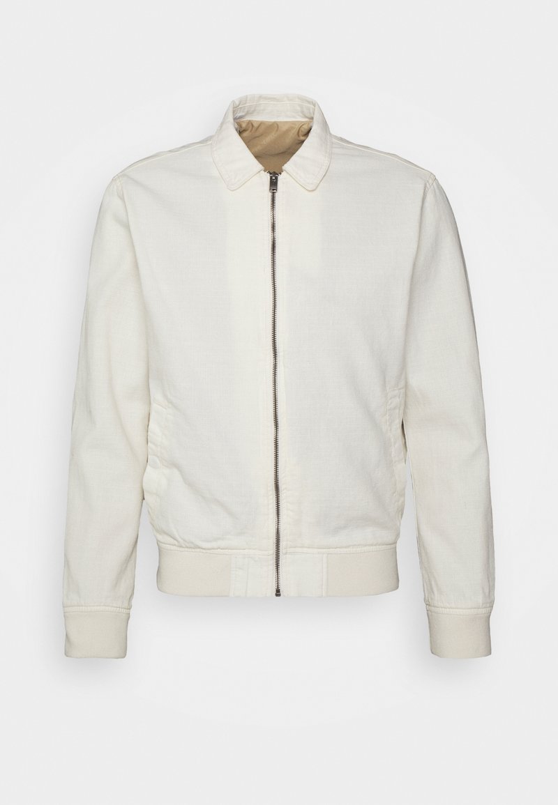 Veste blanche zippée avec col, poignets et ceinture côtelés, montrée de face sur un fond uni.