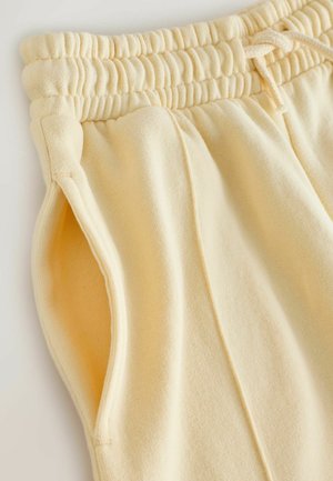 Žute trenirke od mekog materijala, sa rebrastim pojasom s pertlom, bočnim džepovima i vertikalnim šavovima.