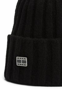 Zwarte gebreide beanie met verticale ribbels, voorzien van een klein rechthoekig metalen logolabel met de inscriptie "TOMMY JEANS."