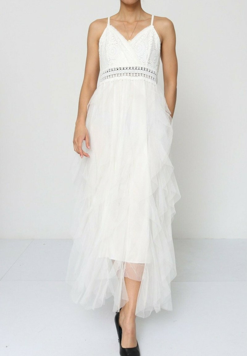 Robe maxi blanche sans manches avec corsage en dentelle, jupe en tulle à volants et bretelles réglables ; présente une texture superposée et une silhouette fluide.