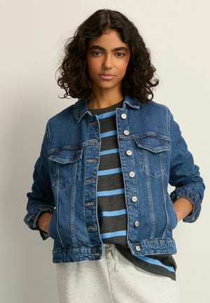 Denim jacket with a classic design, light blue, featuring button closures, chest pockets, and a textured finish, layered over a striped top.
