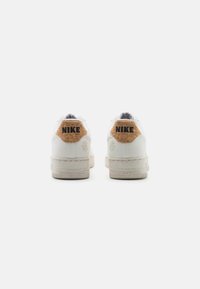 White Nike sneakers featuring a textured cork heel tab with black branding, a cushioned sole, and a clean, minimalistic design.