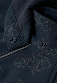 Tissu de veste bleu marine avec une texture douce, présentant des motifs de tracteurs imprimés subtils. Comprend des coutures contrastées et des boutons noirs.