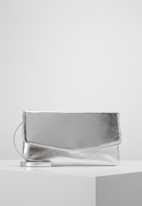 Pochette en métal argenté à texture lisse, avec rabat pliable et bandoulière détachable, présentant des lignes épurées et un design minimaliste.