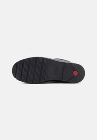 Semelle de chaussure en caoutchouc noir avec un design texturé, présentant des rainures horizontales et un logo rouge circulaire. Construction durable pour une adhérence optimale.