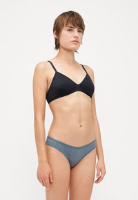 Fekete háromszög bikinifelső vékony pántokkal, szürke mintás bikinitartóval párosítva. Sima textúra, egyszerű design és minimális fém kiegészítők.