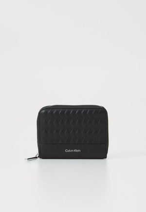 Portafoglio nero con zip, dotato di una texture trapuntata nella parte frontale, lati lisci e logo "Calvin Klein" in rilievo. Forma compatta e rettangolare.