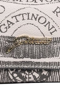 Close-up van textiel met texturen, bedrukt met zwart-witte tekst en geometrische patronen, met een gouden "Gattinoni" logo plaat.