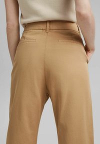 Pantaloni beige con una texture liscia, vita alta e due tasche posteriori. Il tessuto sembra leggero e informale, adatto a varie occasioni.