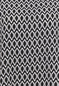Tissu noir et blanc avec un motif géométrique en losange répétitif formant des rangées d'ovales pixellisés.