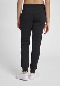 Svarta sweatpants med en åtsittande design, ribbade muddar och ett brett elastiskt midjeband, tillsammans med vita träningsskor.