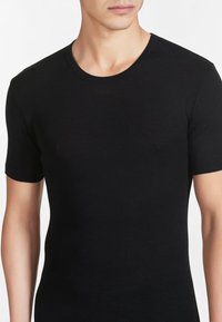 T-shirt nero a maniche corte realizzato in un tessuto morbido e leggero. Collo rotondo e design aderente, che mette in mostra una silhouette semplice e slanciata.