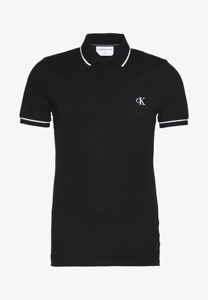 Juoda trumpomis rankovėmis polo marškinėliai su baltais apvadais ant apykaklės ir rankovių, dviem mygtukais ir baltu „cK“ logotipu kairėje krūtinės pusėje.