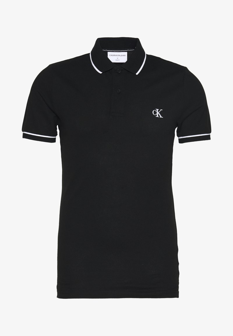 Černá polokošile s krátkým rukávem a bílým lemováním na límci a rukávech, se dvěma knoflíky a bílým logem „cK“ na levé straně hrudi.