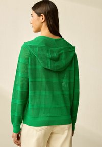 Grön stickad hoodie med horisontella ränder, som har ett strukturerat mönster. Långa ärmar och enfärgad huva med dragsko. Avslappnad passform.