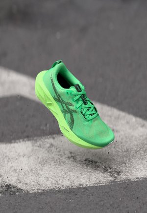 Chaussure de course vert vif en plein air au-dessus d'une route en asphalte avec des marquages de flèches blanches et de petits débris.