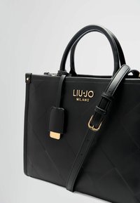 Borsa nera con design trapuntato, logo dorato e dettagli hardware. Presenta doppi manici e una tracolla rimovibile.