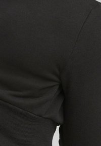 Primo piano di un maglione nero a maglia, con una superficie testurizzata, design aderente e dettagli a coste su polsini e orlo.