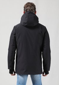 Chaqueta negra impermeable con capucha, con una textura suave y puños elásticos. La parte trasera presenta un diseño limpio y minimalista.