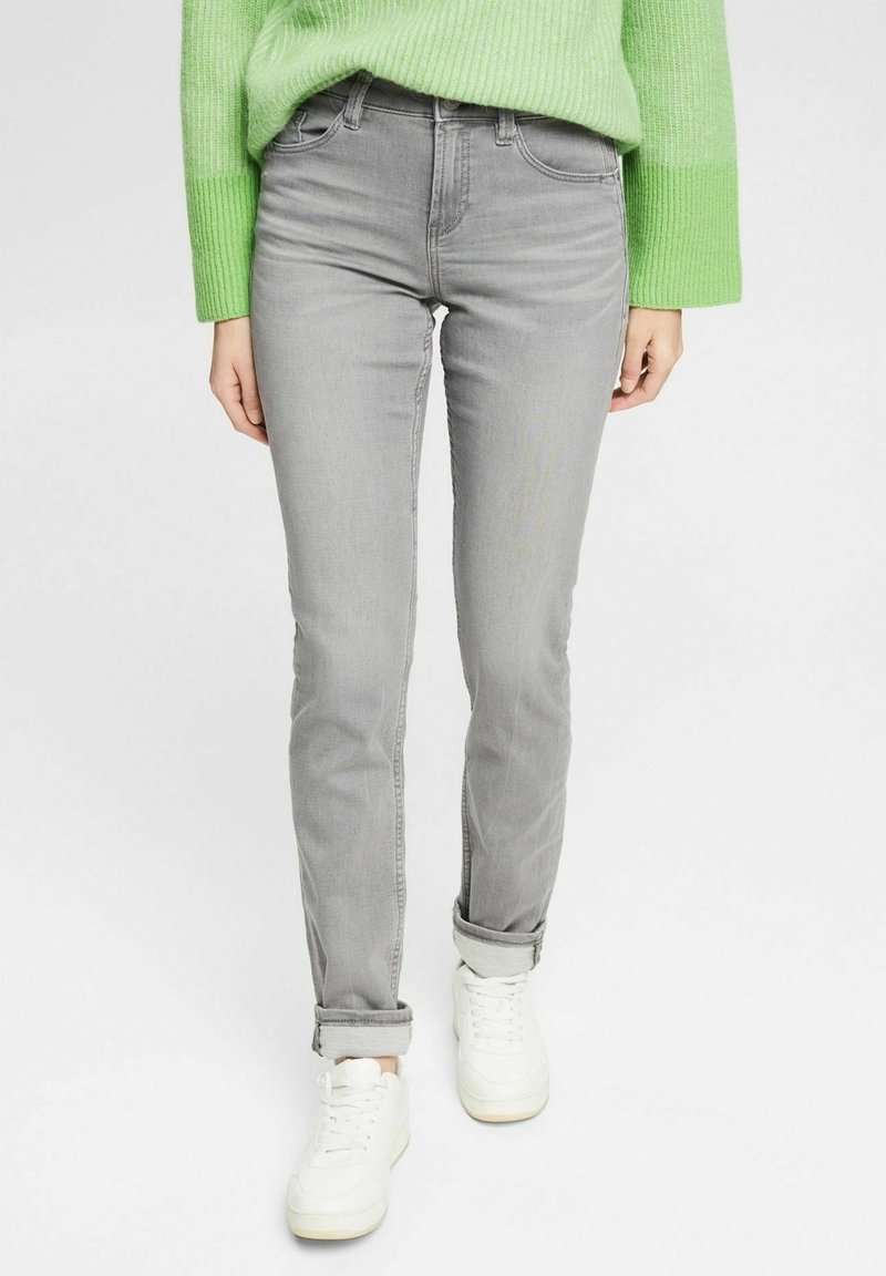 Jean gris slim fit avec revers roulés porté avec des baskets blanches et un pull côtelé vert vif.