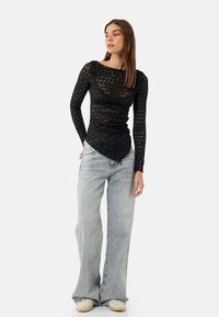 Zwarte kant lange mouwen top met een aansluitende pasvorm, ronde halslijn en asymmetrische zoom, gecombineerd met lichtgrijze wijdlopende jeans.