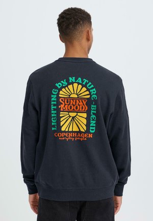 Schwarzer Sweatshirt mit rundem Ausschnitt. Auf der Rückseite befinden sich mehrfarbige grafische Texte und Designs, darunter eine Sonne und der Markenname in fetter Schrift.