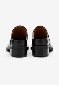 Zwarte leren schoenen met een lage blokhak, gladde textuur, ronde achterkant en beige interieurvoering, met minimalistische designelementen.