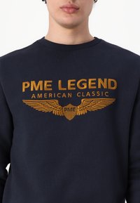 Marineblauwe sweatshirt met gouden borduursels van "PME LEGEND" en vleugels, geribbelde halslijn en een zachte katoenmix.