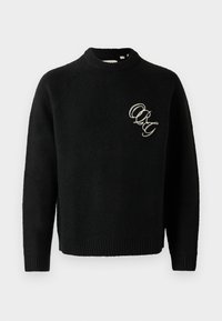 Svart strikket genser med rund hals, med ribbestrikkede mansjetter og nederkant. Broderte bokstaver "ORG" i kontrastfarge på brystet.