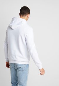 Vit huva sweatshirt med en mjuk textur, ribbade ärmar och nederkant. Bakvy, slät yta, minimalistisk design. Matchad med ljusblå denimjeans.