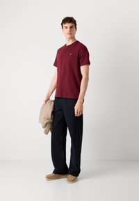 Bordeaux crew-neck t-shirt, bomuldsblanding, parret med navy brede bukser, holder en beige jakke. Brune sko fuldender outfittet.