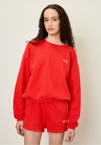 Röd sweatshirt och matchande shorts i mjukt material, med nedhasade axlar och en liten logotyp på bröstet och benet.