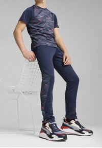 Mörkblå prestations-t-shirt med vågig mönster och röda accenter, kombinerad med matchande joggers med texturerade sidopaneler och märkessneakers.