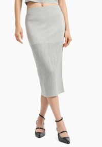 Gonna midi a coste grigia con vita aderente, texture liscia e leggero lucido, abbinata a sandali neri con cinturini.