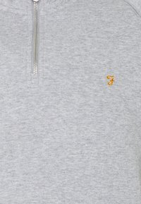 Sudadera gris con cremallera y acabado texturizado. Cuenta con una cremallera plateada y un pequeño logo bordado en amarillo en el pecho.