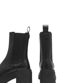 Botas de tobillo negras con un acabado de cuero suave, paneles laterales elásticos y una suela de plataforma gruesa. Presentan un asa y un detalle del logo en la parte trasera.