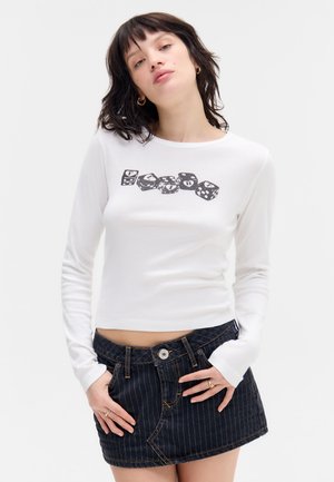Long-sleeve white top with graphic black dice and "FLARE" text, paired with a dark denim mini skirt featuring vertical stripes and a front button.