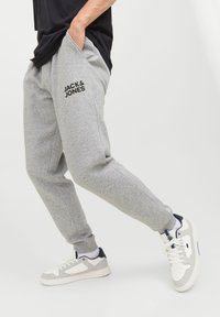 Grey sweatpants featuring side pockets and a black logo "JACK & JONES" on the left thigh, paired with white and grey sneakers.