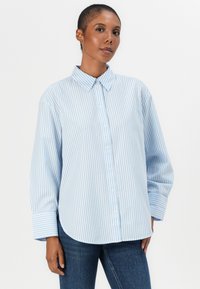 Camicia button-up a righe azzurre e bianche, con colletto, maniche lunghe e polsini larghi; tessuto morbido e vestibilità comoda.