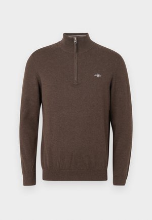 Brown knitted sweater with a high collar and half zip. Features a small logo on the chest and ribbed cuffs and hem. Soft texture.