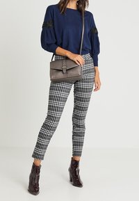 Maglione blu navy con maniche a sbuffo e dettagli in pizzo nero, abbinato a pantaloni a quadri bianchi e neri e stivaletti alla caviglia bordeaux scuro. Borsa grigia.