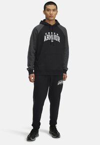 Black hoodie with gray raglan sleeves, featuring "UNDER ARMOUR" text on the front. Paired with matching black sweatpants displaying the logo.