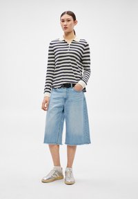 Polo cu mâneci lungi cu dungi și guler bej, asortat cu pantaloni scurți largi din denim albastru deschis. Model purtând adidași argintii și curea neagră.