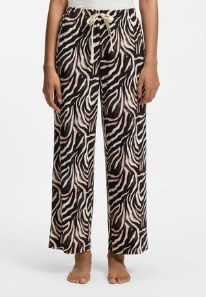 Luźne spodnie w czarno-białe paski zebry, elastyczny pas z beżowym sznurkiem, noszone na boso na białym tle.