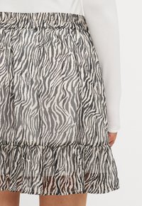 Zebra-mønstrete skjørt i gjennomsiktig stoff med volangkant, med elastisk midje og lett, flytende design. Svart og hvit farge.