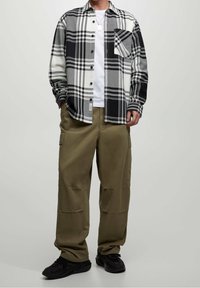Camicia di flanella a quadri bianca e nera, con bottoni e taschino sul petto, abbinata a pantaloni cargo verde oliva. Scarpe da ginnastica nere completano il look.
