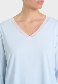 Top azzurro chiaro con scollatura a V caratterizzato da un bordo trasparente, realizzato in un tessuto morbido con maniche lunghe e una vestibilità comoda.