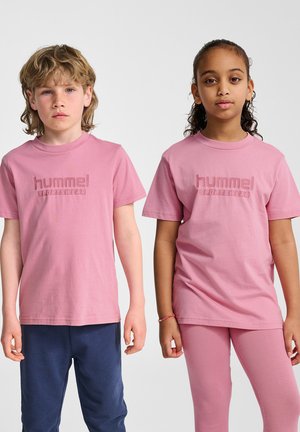 Twee kinderen dragen bijpassende roze katoenen t-shirts met een textuur van het "hummel Sportswear" logo. Het ene kind combineert dit met donkere blauwe broeken, het andere met roze leggings.
