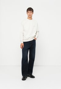 Cream sweatshirt with a round neckline, paired with dark blue wide-leg jeans and black boots, standing against a plain white background.